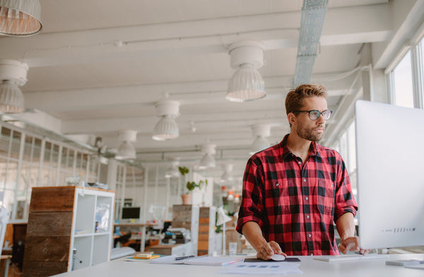 A man working by a well equipped work station of standing desk and ergonomic accessories